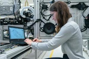 Young woman systems engineer working at lab facility on a laptop surrounded by equipment